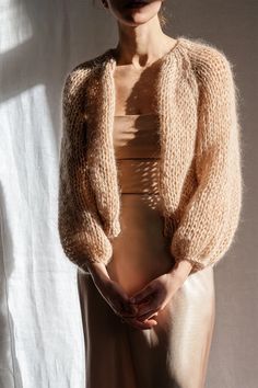 a woman standing in front of a white curtain wearing a tan sweater and beige skirt