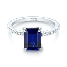 an emerald cut blue sapphire and diamond ring with white diamonds around the band, set in 18k white gold