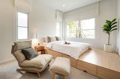 a bedroom with a bed, chair and ottoman in the corner next to two windows