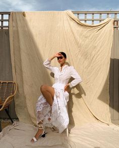 a woman in white dress sitting on a chair with her legs crossed and wearing sunglasses