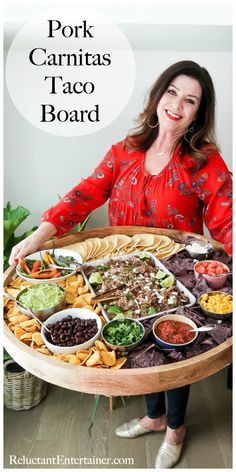 a woman holding a platter full of food with the words pork carnitass taco board