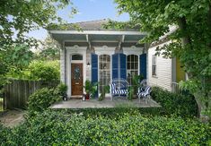 a small house with blue shutters and white trim on the front door is surrounded by greenery