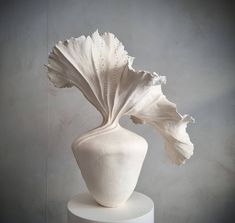 a white vase sitting on top of a table next to a gray wall and floor