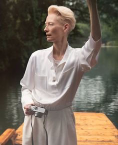 a woman standing on a dock with a camera in her hand and waving to the sky