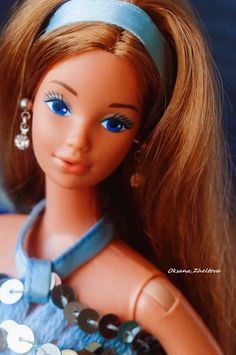 a close up of a doll wearing a blue dress and headband with jewels on it