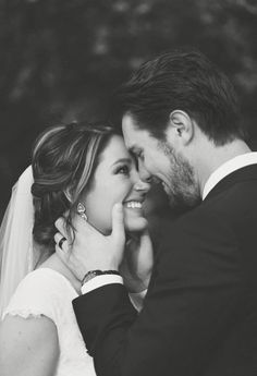 black and white photo of bride and groom smiling at each other with trees in the background