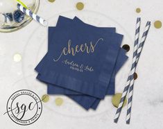 two blue napkins with gold foil lettering on them next to some straws and confetti