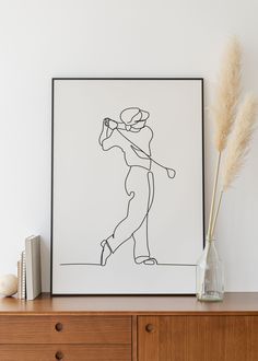 a drawing of a woman holding a baseball bat on top of a wooden dresser next to a vase with dry grass in it