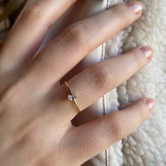 a woman's hand with a diamond ring on top of her finger, resting against a white blanket