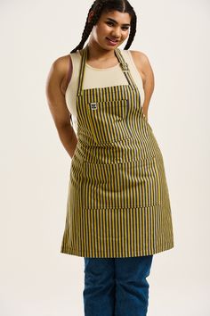 a woman wearing an apron and smiling at the camera with her hands on her hips