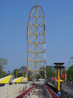 the roller coaster is yellow and red with people sitting on benches in front of it