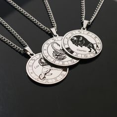 three necklaces with zodiac signs on them sitting next to each other in front of a black background