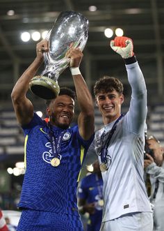 two soccer players holding up their trophies in the air