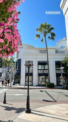 a clock tower on the corner of a street with palm trees in front of it