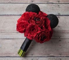 a bouquet with red roses and mickey mouse ears on top of wooden planks, ready to be used as a wedding decoration