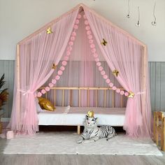 a pink canopy bed with a white tiger laying on the floor in front of it