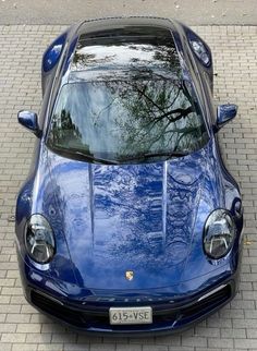 a blue sports car parked in front of a brick sidewalk with trees reflected in the windshield