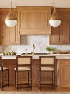 a kitchen with wooden cabinets and marble counter tops, two pendant lights hanging over the island