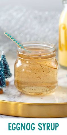 an eggnog syrup in a glass jar with a straw and two small christmas trees next to it