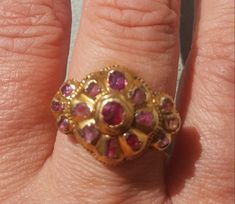 This true antique ring is luscious on all sides. The top of the ring is early 18th century and it is dotted with genuine rubies with a central floral pattern and tri shaped sides. This particular style of ring is typical of the 18th century Iberian area, most likely Portugal. The top was affixed on to a 14k gold ring  (marked 14k),shank that is elaborately hand chased and custom made by a very competent gold smith to mirror the side profiles of the ring head. The shank is marked 14k and is presently a size 6 1/2. The shank is substantial in its weight and thickness. The style of the ring suggests this work was done in 1920's. The central ruby has been replaced as well as one of the petal rubies, but this is nicely done.  A very nice ring that is very comfortable to wear. Follow me on insta Traditional Hallmarked Ruby Ring For Ceremonies, Ornate Gold Ruby Ring, Traditional Oval Ruby Ring, Traditional Yellow Gold Ruby Ring, Ornate Gold Ring With Ruby, Ornate Gold Rings With Ruby, Traditional Hallmarked Ruby Ring, Traditional Ruby Ring For Formal Occasions, Antique Multi-stone Ruby Ring