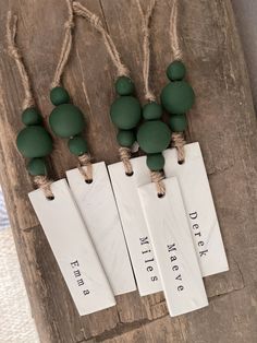 three tags are attached to some string on a piece of wood with green beads hanging from them