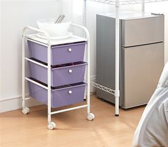 a white and purple cart with three drawers next to a refrigerator in a room that has wood floors