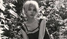 a black and white photo of a woman sitting in front of some bushes with her hands on her knees