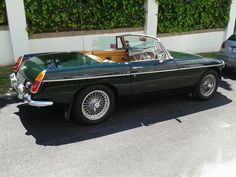 an old green convertible car parked in front of a building with two other cars behind it