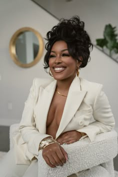 a woman sitting on top of a white chair in front of a mirror and smiling