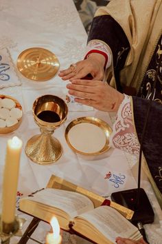 two people sitting at a table holding hands over an open book with candles in front of them