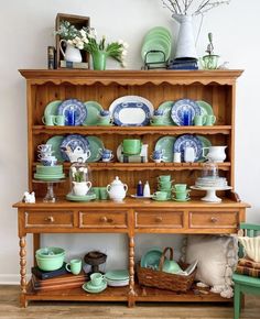 a wooden china cabinet filled with lots of plates and cups next to a green chair