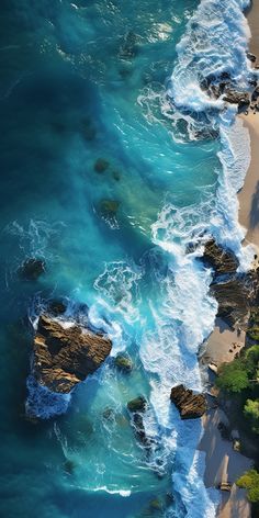 an aerial view of the ocean and beach with rocks in the foreground, looking down