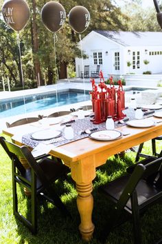 a table with plates and glasses on it in front of a pool surrounded by balloons