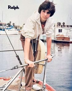 a man standing on top of a boat holding onto a metal bar while wearing brown pants