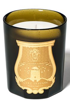 a candle that is sitting in front of a white background with a gold emblem on it