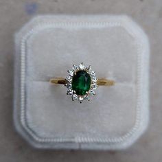 a ring with a green stone surrounded by small white diamonds in a velvet box on the floor