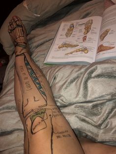 a person with tattoos on their legs laying in bed next to an open book