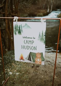 a welcome sign to camp hudson with a bear and tent in the woods behind it