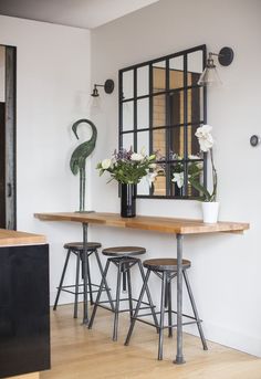 a dining table with four stools in front of it and a mirror on the wall