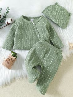 a baby's green outfit and hat laying on top of a white rug