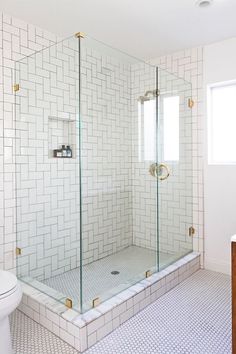 a bathroom with a toilet and a walk in shower next to a white tiled wall