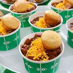 several green cups filled with chili and cornbreads on top of a football field