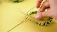 someone is making a bracelet with green string and beads