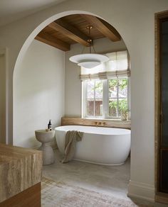 an arched doorway leads to a large white bathtub in the middle of a bathroom