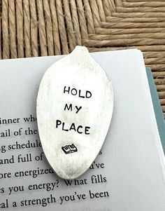 a spoon with writing on it sitting next to an open book that says hold my place