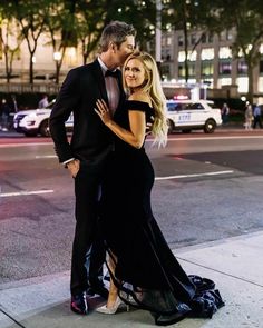 a man and woman in formal wear standing on the side of a street at night