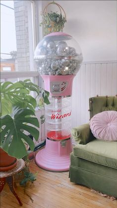 a pink machine sitting in front of a window next to a chair and potted plant