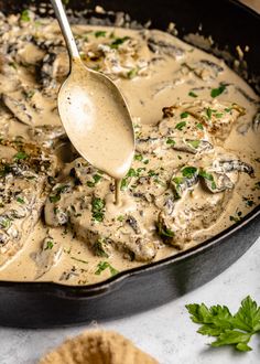 a skillet filled with mushrooms and gravy being stirred with a ladle