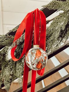 a christmas ornament hanging from the side of a staircase with red ribbon on it