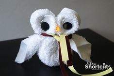 an owl made out of toilet paper sitting on top of a black table next to a yellow ribbon